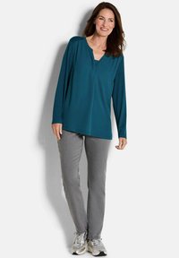 Tiefblaue Langarmbluse mit V-Ausschnitt, kombiniert mit hellgrauen Hosen. Weiße Sneaker mit metallischen Akzenten runden das Outfit ab.