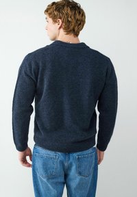 Granatowy sweter dzianinowy o luźnym kroju i ściągaczach, zestawiony z jasnoniebieskimi spodniami typu straight-leg z tylnymi kieszeniami.