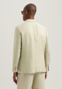 Helle beige Leinenjacke mit taillierter Passform, Reverskragen, dreiknöpfigem Verschluss und seitlichen Schlitzen, von hinten gezeigt.