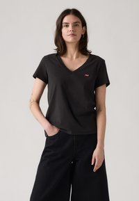 T-shirt noir à col en V en coton avec des manches courtes, arborant un petit logo rouge de Levi's sur la poitrine. Assorti à un large pantalon noir.