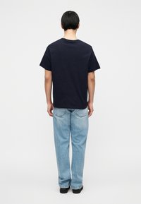 Μπλε βαμβακερό t-shirt με κοντά μανίκια και στρογγυλό λαιμόκοψη, συνδυασμένο με ανοιχτό μπλε τζιν παντελόνια που διαθέτουν πίσω τσέπες και άνετη εφαρμογή.