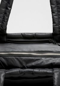 Crni jastučić s glatkom teksturom, koji ima istaknut srebrni zatvarač i dvostruke ručke. Uključuje siguran odjeljak sa zatvaračem.