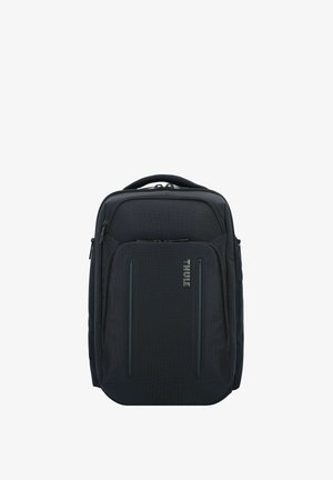 Sac à dos en tissu noir avec une poignée rembourrée, des compartiments zippés, un motif subtil et un détail de logo sur le devant.