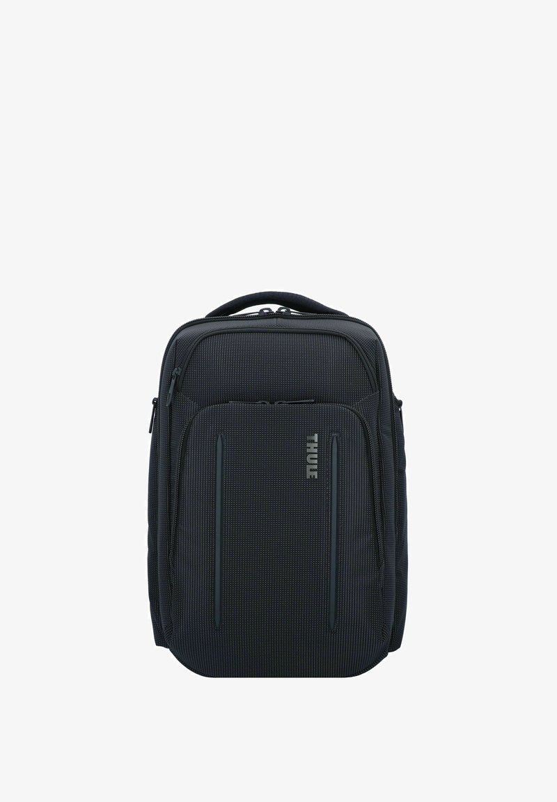 Sac à dos en tissu noir avec une poignée rembourrée, des compartiments zippés, un motif subtil et un détail de logo sur le devant.