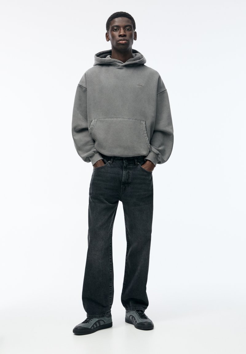 Felpa grigia in cotone con tasca frontale, abbinata a jeans dritti grigio scuro. Sneakers nere con dettagli grigi completano il look.