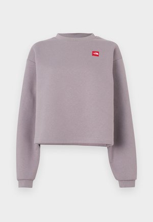 Lila kort sweatshirt med långa ärmar, ribbad halsringning och en liten röd logotypmärke på bröstet. Mjukt material med en slät textur.