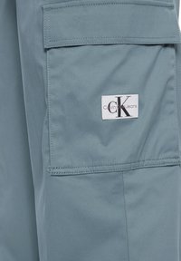 Pantaloni cargo azzurri chiari realizzati in tessuto morbido, con una tasca piatta e un'etichetta con il logo Calvin Klein Jeans cucita di lato.