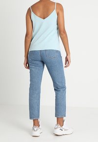 Ljusblå slim-fit tanktop med tunna axelremmar, kombinerad med högmidjade blåjeans och vita sneakers med grå detaljer.