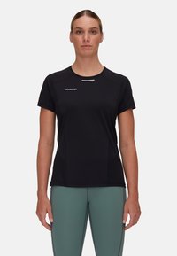 Svart atletisk t-shirt med korta ärmar, fukttransporterande material, diskret logotyp på bröstet och figurnära design, matchad med gröna tights.