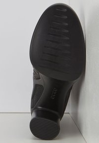 Sole di scarpa nera con grip in gomma texture e righe orizzontali. Il lato presenta una sovrapposizione in materiale intrecciato con un design a ritaglio.