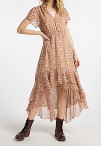 Robe florale dans des tons chauds avec des couches volantées, des manches courtes, un col en V et une taille smockée. Associée à des bottes brunes à lacets.