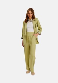 Bledě zelený upravený blejzr a kalhoty s vysokým pasem, doplněné bílým topem a šátkem s potiskem. Celkový vzhled doplňují neformální boty.