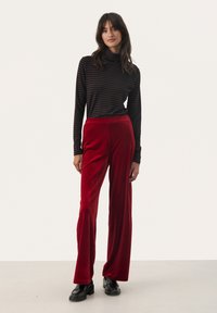 Black and brown striped turtleneck paired with wide-leg red velvet pants. Model stands with hands on hips in black platform shoes.