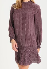 Långärmad klänning i vinröd med en strukturerad mönster, med en volangkant och en hög halsringning med rynkade detaljer på ärmarna.