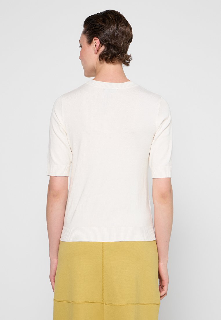 Top en tricot crème à manches courtes avec un col rond, texture côtelée et silhouette ajustée, associé à une jupe texturée jaune clair.