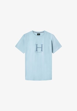 Camiseta de algodón azul claro con mangas cortas y cuello redondo, que presenta un gran logo gris con la letra "H" y el texto "HACKETT" debajo. Textura suave.