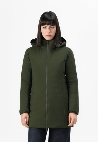 Femme portant un manteau d'hiver à capuche zippé, vert olive, les mains détendues sur les côtés, contre un fond blanc uni.