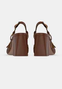 Sandales à talons brunes avec une finition en cuir lisse, dotées d'un talon large et carré, d'une bride à la cheville et d'accents de quincaillerie dorée.