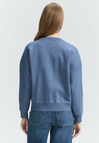 Felpa blu con collo a giro, spalle ribassate e polsini a costine. Realizzata in tessuto testurizzato, presenta una vestibilità morbida e un design cropped.