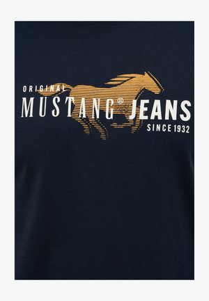 Camiseta de algodón azul marino con un gráfico dorado de un caballo y texto blanco que dice "Original Mustang Jeans Desde 1932". Textura suave.