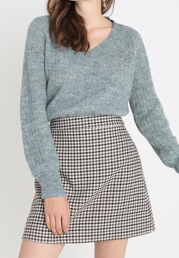 Pull bleu clair à col en V, manches longues, tricot texturé, associé à une mini-jupe imprimée pied-de-poule noir et blanc.