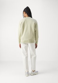 Lys grønn genser med rund hals og ribbede mansjetter, sammen med hvite bukser. Joggesko med grå og beige detaljer.