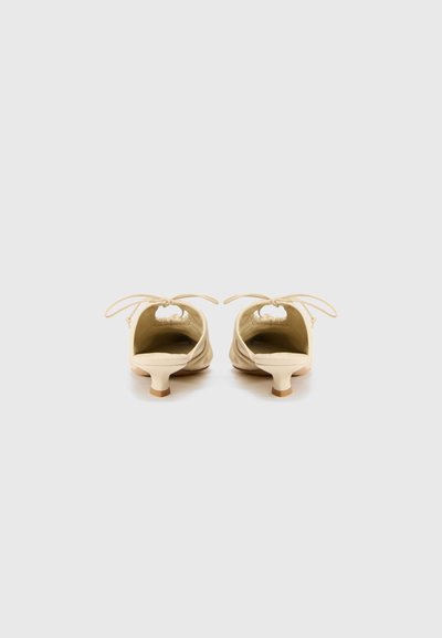 Zapatos beige de textura suave con punta redondeada; presentan un tacón bajo y curvado, además de cordones ajustables en la parte posterior.