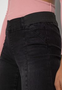 Pantalones de mezclilla negros con una cinturilla negra acanalada, diseño ajustado y textura ligeramente elástica, combinados con una blusa rosa acanalada.