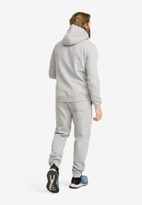 Grå hoodie och jogger-set i mjukt tyg. Har en huva, ribbade ärmslut och en avslappnad passform. Bärs med blå och svarta träningsskor.
