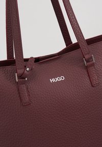 Sac cabas en cuir texturé bordeaux avec double anses et logo "HUGO" argent embossé sur le devant.