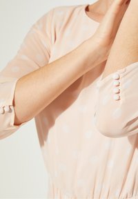 Rosa gepunktetes Kleid aus leichtem Stoff mit rundem Ausschnitt und Knopfdetails an den Ärmelbündchen. Glatte Textur.