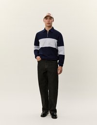 Námornícke a svetlosivé zip-up pulóver s golierom, s textom. Čierne široké nohavice a svetlá čiapka dotvárajú outfit.