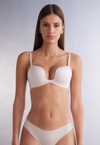 Beige formad bh med tunn justerbar axelrem och slät yta; matchas med sömlös bikinitrosa. Enkelt design.