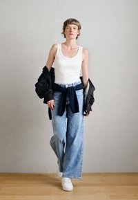 Άσπρο αμάνικο μπλουζάκι, μαύρο μπουφάν bomber, φαρδιά ανοιχτό μπλε τζιν και λευκά αθλητικά παπούτσια. Casual, άνετη εφαρμογή με απαλή υφή.