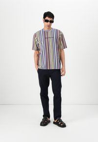 Striped cotton t-shirt with horizontal lines in lavender, red, navy, and cream. Paired with dark navy pants and black sandals.