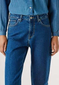 Světle modré džíny s vysokým pasem, pěti kapsami, zipem a kontrastním prošíváním. Rovný přední díl s mírným vyblednutím.