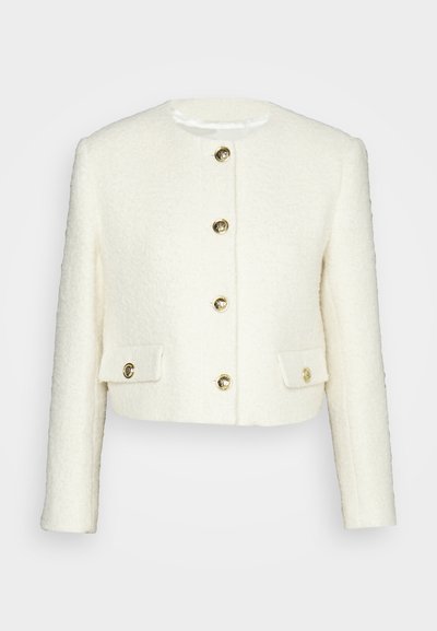 Veste blanche courte en tissu texturé, dotée d'un col rond, de cinq boutons dorés et de deux poches à rabat avec boutons dorés.