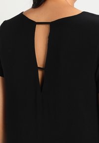 Robe noire avec un design de dos en trou de serrure, manches courtes et une texture de tissu lisse. Style simple et minimaliste.