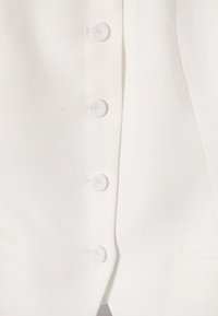 Gros plan sur le devant d'une veste blanche avec quatre boutons ronds recouverts de tissu alignés verticalement.