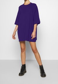 Fioletowa, oversize t-shirt z okrągłym dekoltem i krótkimi rękawami, w połączeniu z czarnymi, sznurowanymi botkami. Gładki materiał, prosty design.