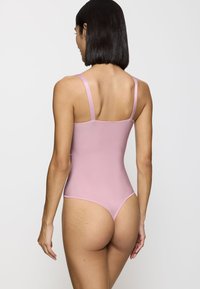 Body rosa con tirantes ajustables, textura suave, aberturas de pierna altas y cobertura mínima en la parte posterior. Diseño simple sin patrones ni acentos.