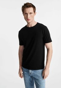 Czarny t-shirt z krótkim rękawem, okrągły dekolt, materiał bawełniany, z małym emblematem na piersi, w połączeniu z jasnoniebieskimi dżinsami.