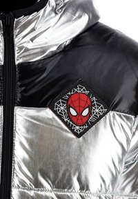 Silver puffer jacket featuring black accents, a zip closure, and a red Spider-Man patch on a diamond-shaped embroidered background.