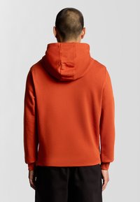 Sudadera naranja con capucha ajustable, mangas largas y una tela suave y texturizada. Diseño simple sin logotipos ni patrones visibles.