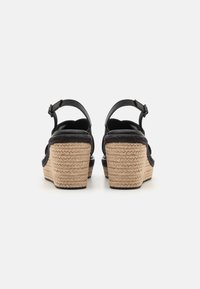 Černé kožené platformové sandály s pleteným jutu na podpatku, s nastavitelným páskem kolem kotníku a texturovaným povrchem pro lepší úchop.