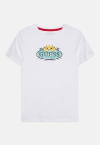 Valkoinen puuvillateepaita, jossa on elävä grafiikka keltaisista kukista ja teal-väreistä, jonka päällä on koristeellinen "GUESS"-teksti.