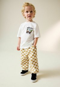 Camiseta blanca con un gráfico colorido que dice "DÍAS SALVAJES", combinada con pantalones a cuadros amarillos y blancos y zapatillas negras.