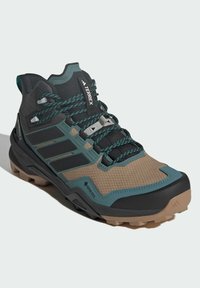 Wysokie buty trekkingowe w kolorze czarnym i brązowym z akcentami w kolorze turkusowym. Charakteryzują się teksturowaną powierzchnią, pewnym systemem sznurowania oraz solidną podeszwą zapewniającą przyczepność.