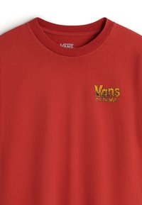 Rød bomulds T-shirt med ribbet rund hals. Den har et broderet "Vans Off The Wall" logo i gul på brystet.