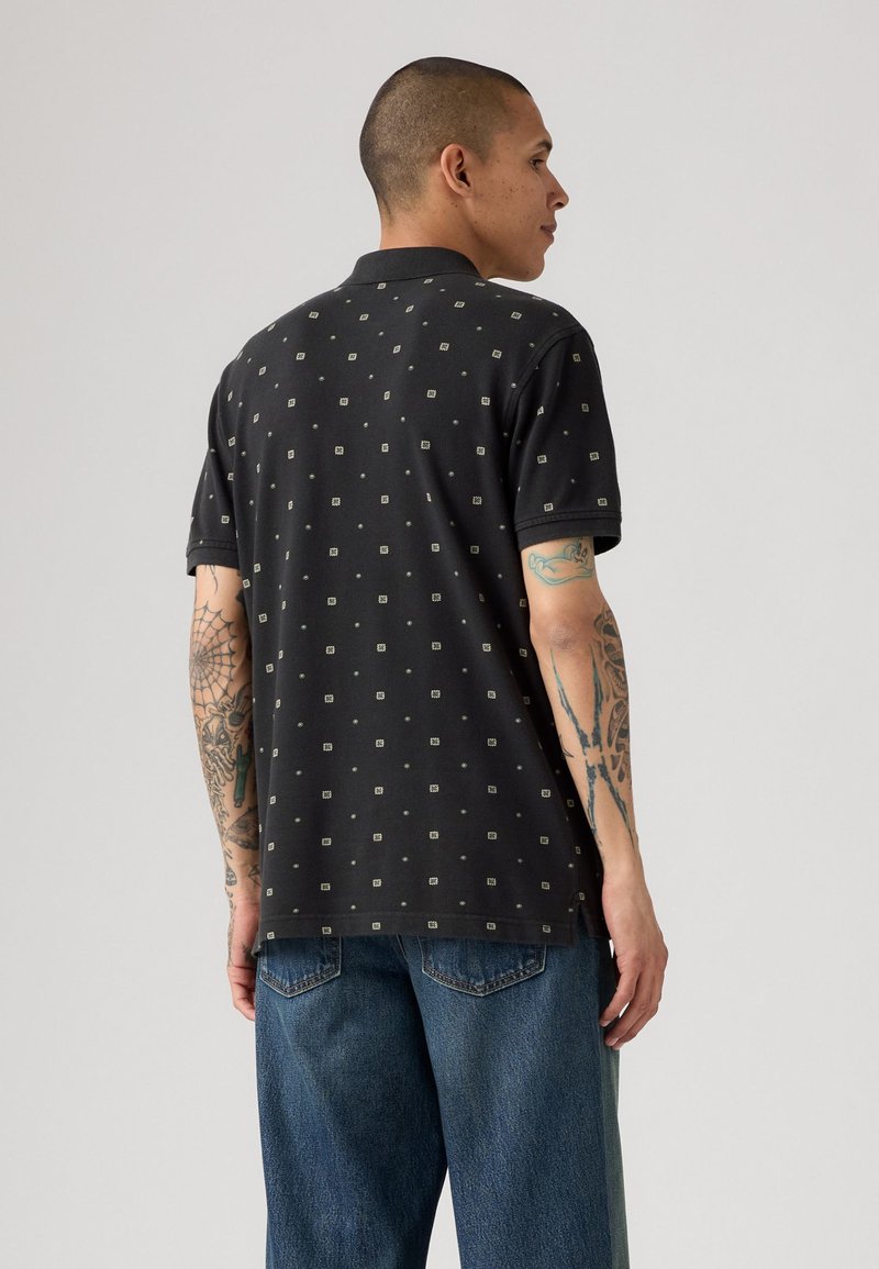 Schwarzes Polohemd mit kleinen Quadratmuster, kurzen Ärmeln und Kragen, kombiniert mit blauen Denim-Jeans. Verfügt über eine lässige Passform und ein entspanntes Design.